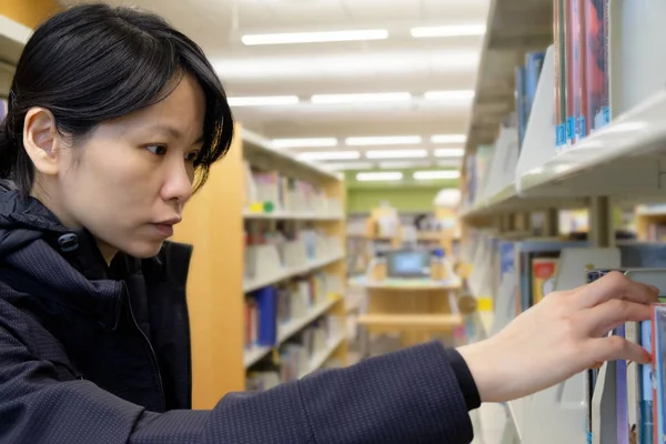 Retrato de una chica asiática seria en la biblioteca buscando un libro — Foto de Stock