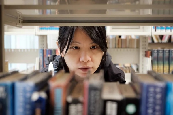 Retrato de una chica asiática seria en la biblioteca buscando un libro — Foto de Stock