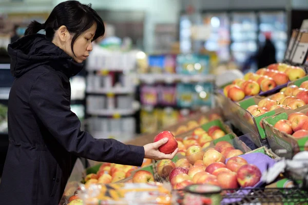 Asian woman choosing fresh apple in grocery store — Stock Photo, Image