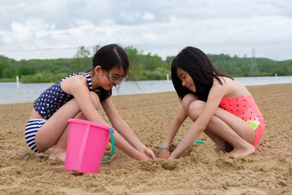 Two little Asian girls playing sand at beach — Stock Photo, Image