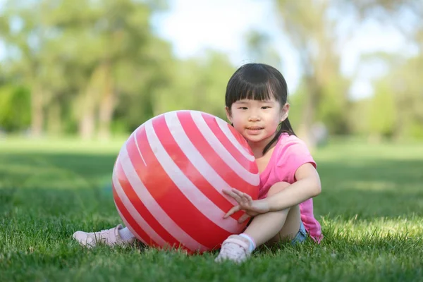 Kleine Aziatische meisje pose met rode bal in Park — Stockfoto