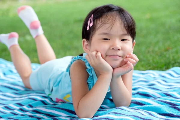Little toddler girl laying on towel in the grass on a summer day — Stock Photo, Image