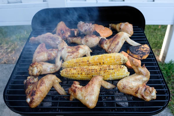 Letní barbecue vaření nad horkým ohněm s kuřecími křídly, stehny a kukuřicí — Stock fotografie