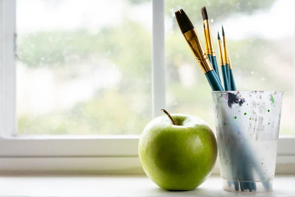 Brosses à peinture avec une pomme verte à côté de la fenêtre — Photo