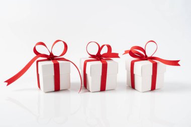 Noel, yeni yıl, sevgililer günü ya da doğum günü temalı yansıtıcı beyaz yüzeye kırmızı saten kurdeleyle bağlanmış üç kare beyaz hediye kutusu.