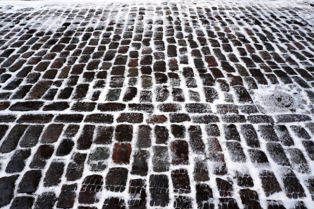 Old traditional stone pavement covered with snow in winter.