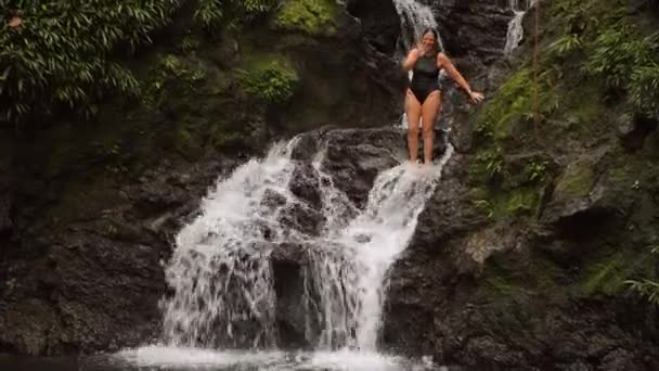 Woman jumping in a pool below a waterfall — Stock Video