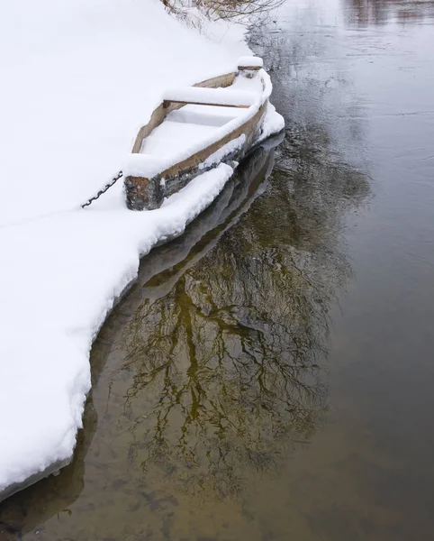 Wood boat covered with snow on the shore of winter river