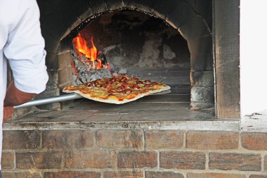pizza coming out of wood fired pizza oven in restaurant clipart