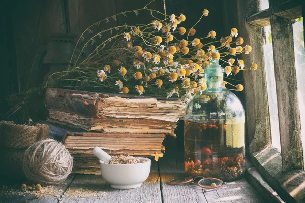干疗草药砂浆 精油瓶或输液器 旧书和一束干甘菊植物 — 图库照片