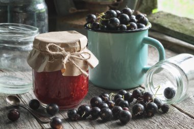 Siyah kuş üzümü reçeli, emaye kupa Olgun siyah kuş üzümü ve retro köyü evin içinde tahta masada boş cam kavanoz kavanoz.