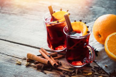 Glass mugs of mulled wine with spices and citrus fruits on wooden table with autumn leaves. Copy space for text. clipart