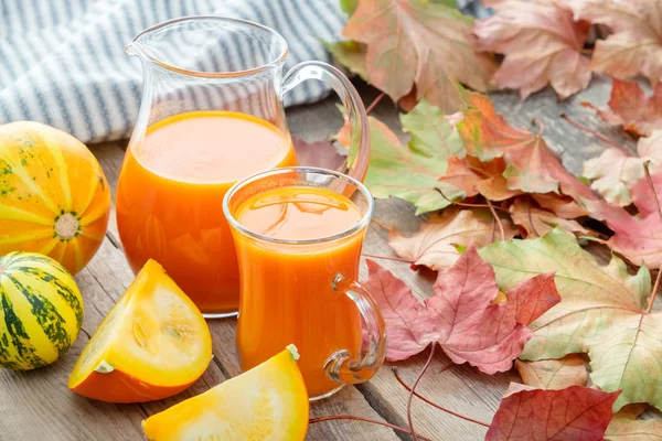 Glazen kan en kopje pompoen juice, pompoenen en gevallen esdoorn bladeren. — Stockfoto