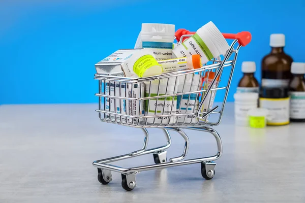 Mini shopping cart full of homeopathic remedies on blue background. Concept of buying homeopathic drugs.