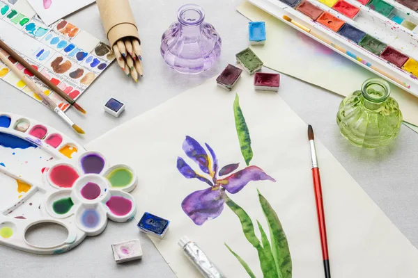 Desenho em aquarela - Flor de íris - e equipamento artístico na mesa. Vista superior . — Fotografia de Stock