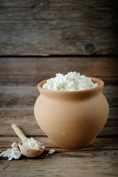 Cottage cheese in brown rustic clay pot and wooden spoon. — Stock Photo, Image