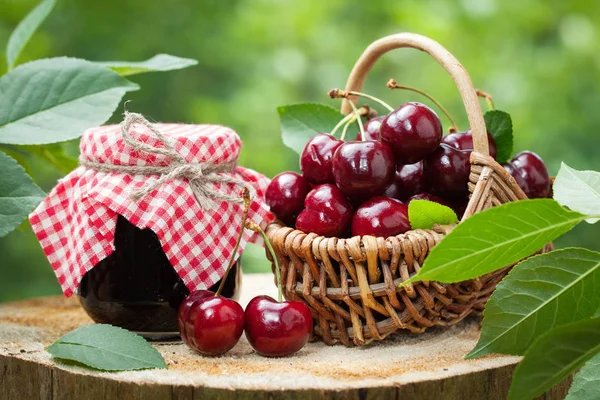Tarro de mermelada y cesta de cerezas dulces sobre fondo en jardín al aire libre . — Foto de Stock