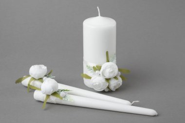 Gri arka planda beyaz güllerle süslenmiş üç mum.