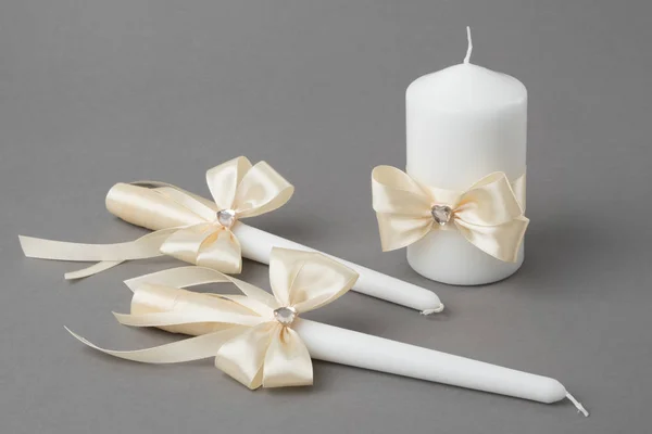 Tre candele decorate con fiocchi di seta beige su sfondo grigio . — Foto Stock