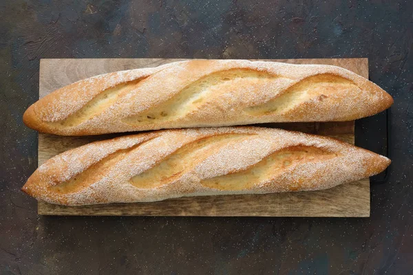 Two freshly baked baguettes on cutting board. Top view.