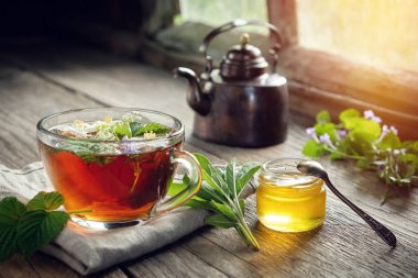 Masa üzerinde çeşitli şifalı bitkiler ve otlar, sağlıklı bitkisel çay bardağı, bal kavanozu ve Vintage bakır çay su ısıtıcısı.