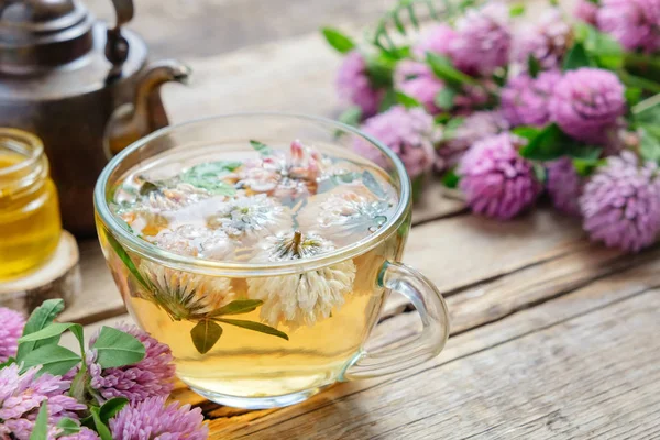 Red clover flowers, healthy herbal tea cup, honey jar and vintage copper tea kettle on table. — Stock Photo, Image