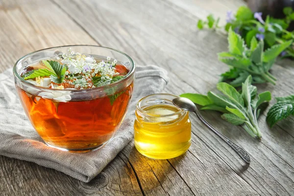 Taza de té de hierbas saludable, tarro de miel y hierbas medicinales en la mesa de madera vieja . — Foto de Stock