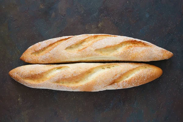 Dos baguettes recién horneadas sobre fondo marrón oscuro. Vista superior . — Foto de Stock