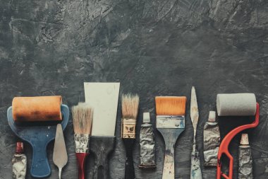 Sanatçı boya fırçaları, fırça silindirleri, palet bıçakları, gri beton arka plan üzerinde yakın çekim boya tüpleri.