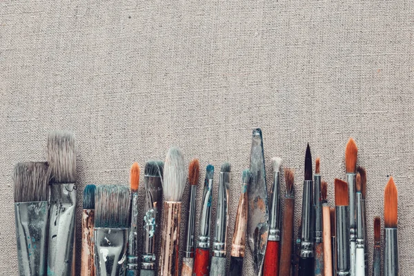 Fila de pinceles de artista y cuchillo de paleta sobre tela de lino . — Foto de Stock