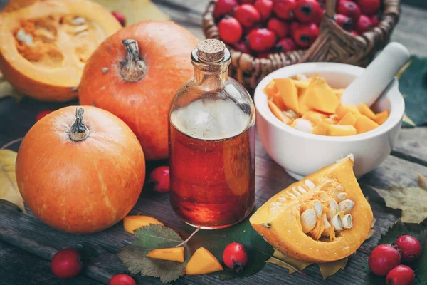 Pumpkin seeds oil bottle, pumpkins, mortar and basket of hawthorn berries — Stock Photo, Image