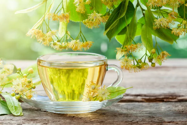 Copo de vidro de chá saudável com flores de tília na tábua de madeira, flores de árvore de limão . — Fotografia de Stock