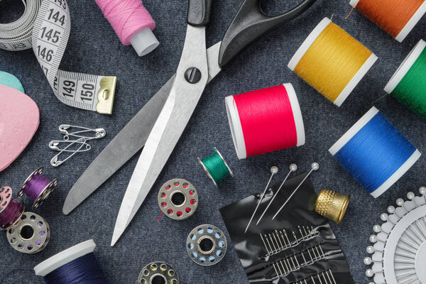 Швейные изделия: пошив ножниц; измерительная лента; наперсток; катушки ниток, включая булавки, иглы и швейные аксессуары на швейной ткани. Вид сверху
. 