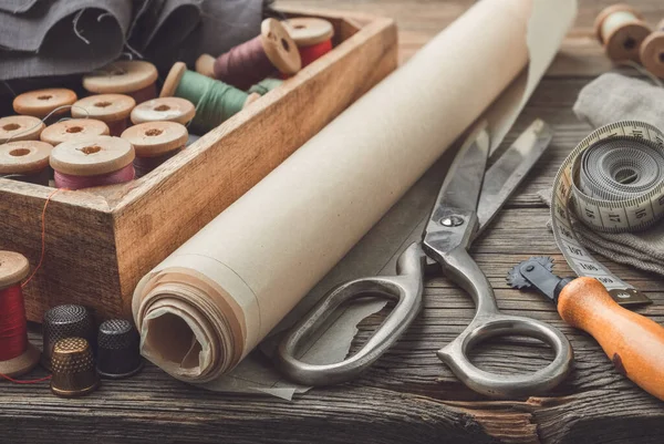 Artículos de costura: tijeras de sastrería retro, cinta métrica, dedal, carretes vintage de hilo en caja de madera, patrones en papel y cuchillo de corte a medida . — Foto de Stock