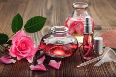 Gül çiçeği, aşılanmış su ve gerekli yağ veya gül karışımı şişesi, sprey şişedeki aromalı su, pembe kil tozu, cam spatula ve evde kozmetik ürünler üretmek için küçük huni.