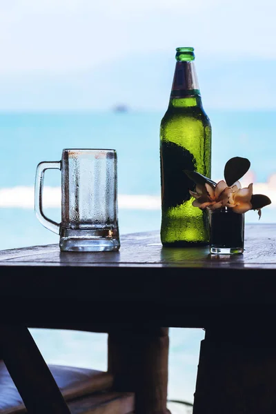 Bottiglia di birra verde e tazza con gocce sul tavolo di legno — Foto Stock