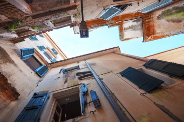 Sosyal konutların eski boyanmış duvarları, harabeler, pencere perdeleri olan pencereler, gökyüzünün bir parçası, güney kasabası, yukarı doğru manzara. 