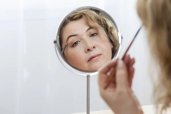 Beautiful Caucasian woman looking in the mirror and applying mak — Stock Photo, Image