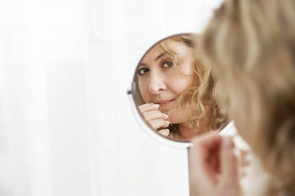 Mooie rijpe blanke vrouw op zoek in de spiegel Stockfoto