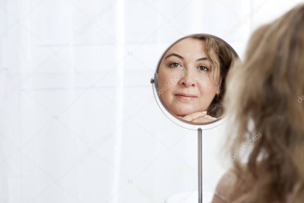 Beautiful mature Caucasian woman looking in the mirror