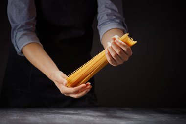 Karanlık arka plandaki kadının ellerinde bir demet spagetti. İtalyan yemeği konsepti.