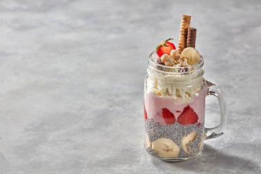 kavanoz ile yoğurt, çilek, muz ve chia muhallebi tatlı katmanlı, bisküvi ile dekore edilmiş ve beton zemin üzerine krem şanti