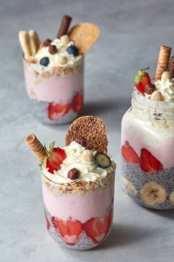 katmanlı tatlı ile bardak yoğurt, çilek, muz ve chia puding, bisküvi ile dekore edilmiş ve beton zemin üzerine krem şanti