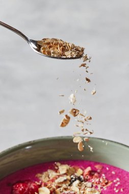 Yulaf gevreği bir kaşık gelen bir kase taze meyve smoothies ile bir tabak içine dökülür. Sağlıklı bir kahvaltı hazırlanması