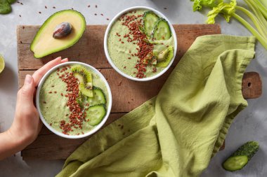 avokado ve flaxseeds yeşil peçete ile sevimli bir ahşap tahta üzerinde kadının elinde tepesinde kivi ve salatalık güler yüzlü kase Kahvaltı, yat. Süper yiyecek