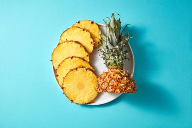 Metin, üstten görünüm altında boşluk ile mavi bir arka plan üzerinde izole bir beyaz yuvarlak plaka üzerinde yeşil bir top ile dilimlenmiş ananas sarı halkalar