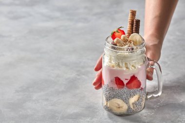 yoğurt, çilek, muz ve chia pudingi, katmanlı tatlı kavanozu tutan el bisküvi ile dekore edilmiş ve beton zemin üzerine krem şanti