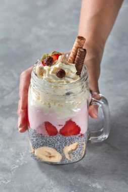 yoğurt, çilek, muz ve chia pudingi, katmanlı tatlı kavanozu tutan el bisküvi ile dekore edilmiş ve beton zemin üzerine krem şanti