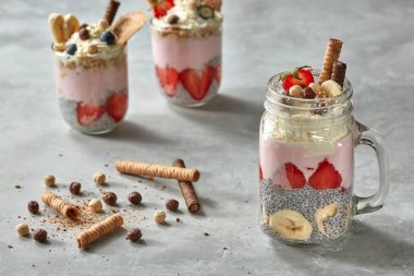 kavanoz ile yoğurt, çilek, muz ve chia muhallebi tatlı katmanlı, bisküvi ile dekore edilmiş ve beton zemin üzerine krem şanti