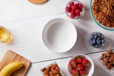 sağlıklı bir kahvaltı için-malzemeler granola, fındık, ahududu, çilek, yaban mersini kase Beyaz ahşap zemin üzerinde. Üstten görünüm, kopya alanı